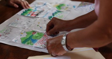 Manos de mujer colocando su dibujo hecho a mano en la mesa al lado de otros dibujos de montañas y ríos.